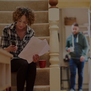 woman sitting on stair reviewing insurance policy, man walking toward her with coffee